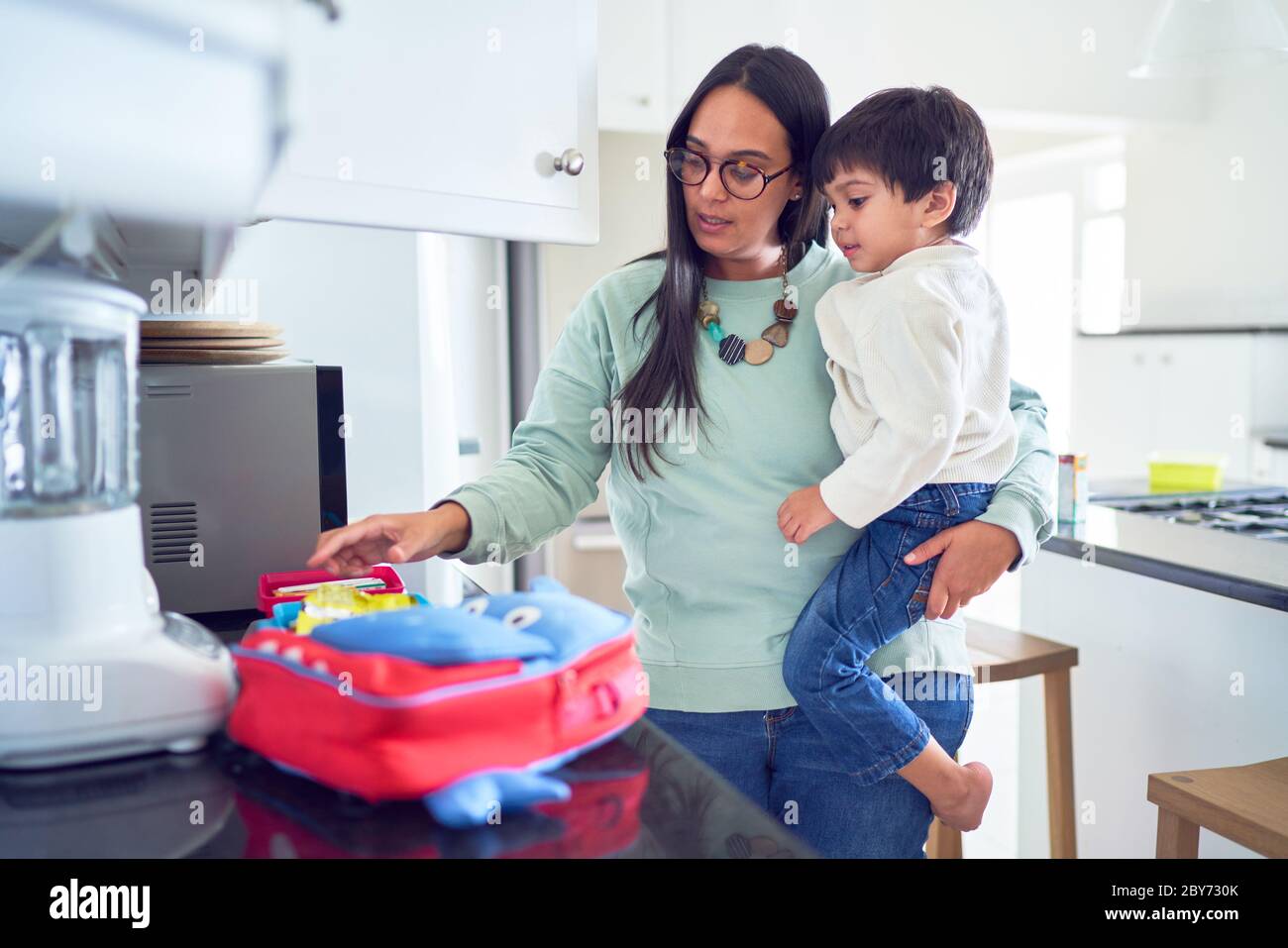 Mother holding son and preparing school lunch in kitchen Stock Photo