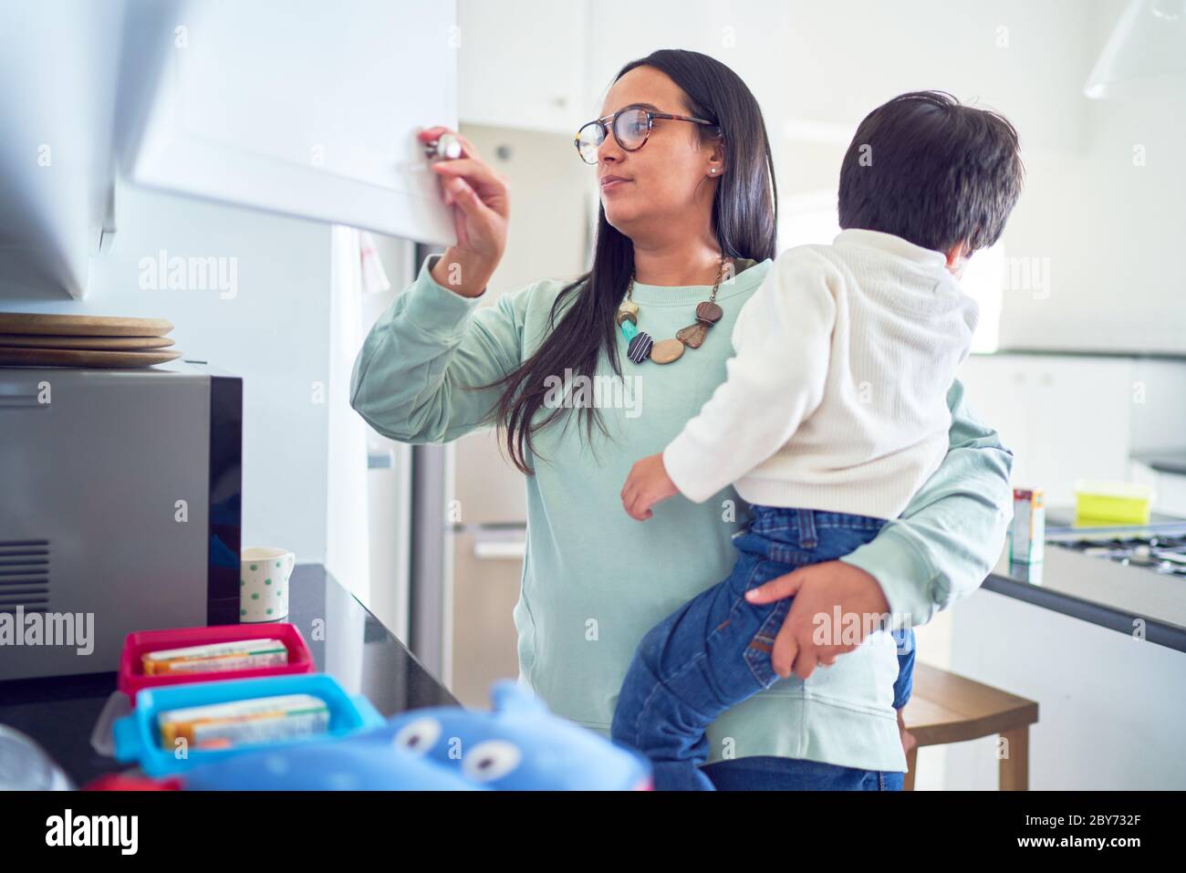 Mother holding son and preparing lunches in kitchen Stock Photo