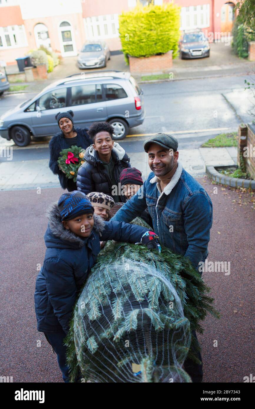 Portrait happy family carrying Christmas tree in driveway Stock Photo