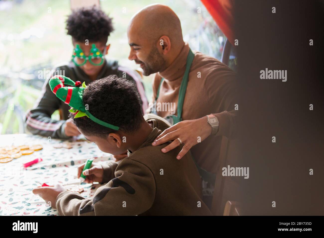 Father and sons decorating Christmas cookies at table Stock Photo