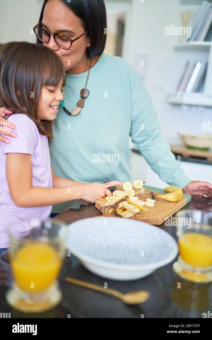 Affectionate mother kissing daughter cutting banana in kitchen Stock Photo