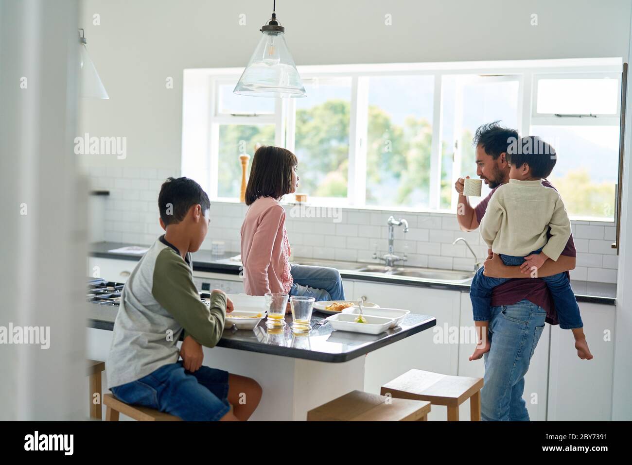 Father and kids eating takeout food in kitchen Stock Photo