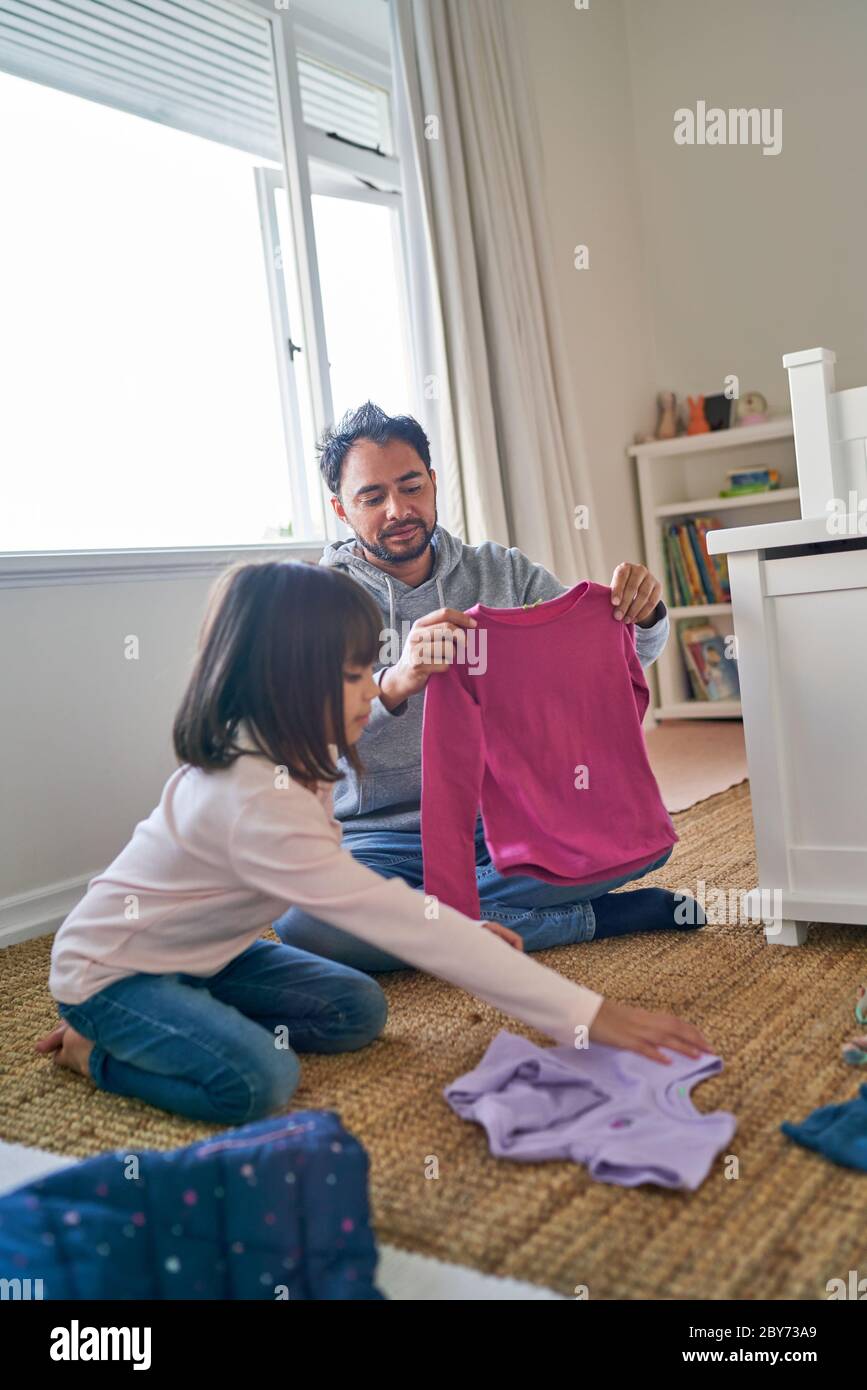 Father helping daughter fold clothes in bedroom Stock Photo
