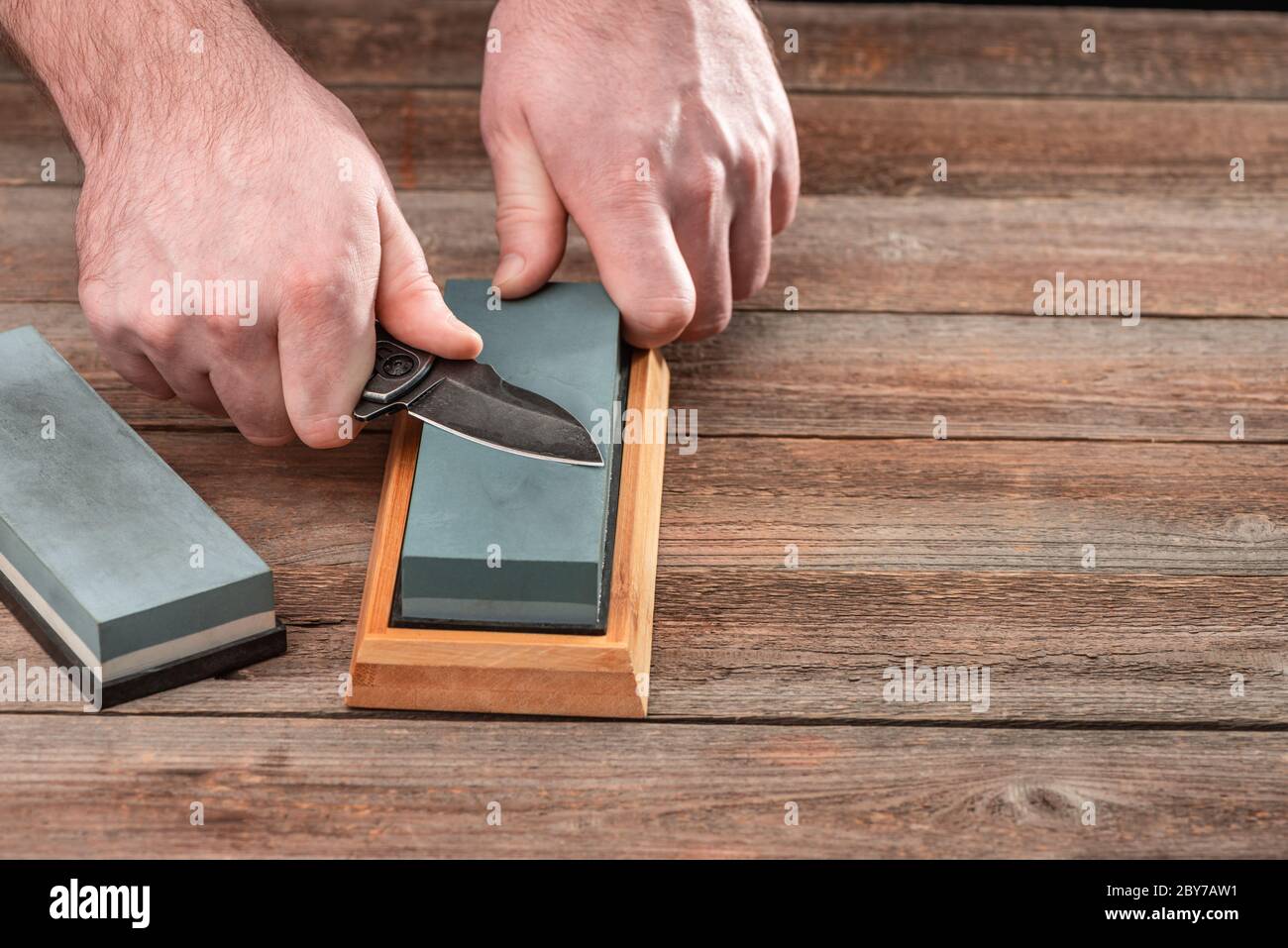 Man sharpening his pocket knife with a whetstone on a rustic wooden table  Stock Photo - Alamy