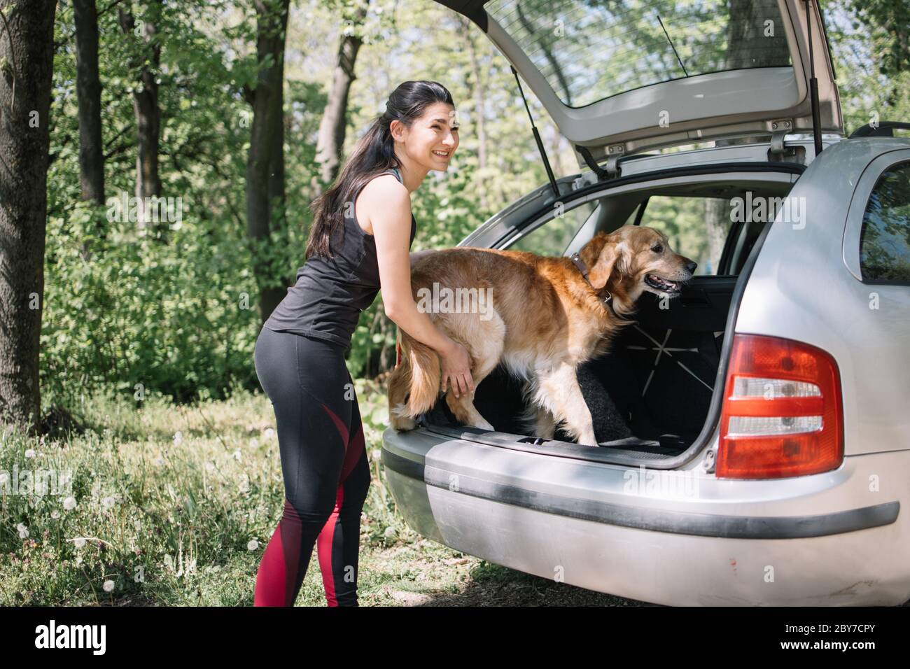 Happy girl putting dog into car's trunk Stock Photo Alamy