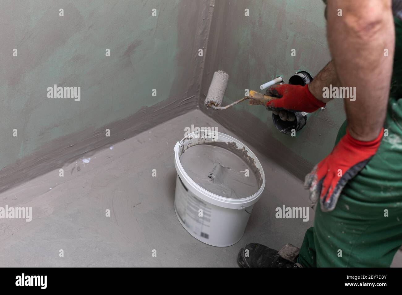 A construction worker soaks a paint roller in a bucket full of liquid