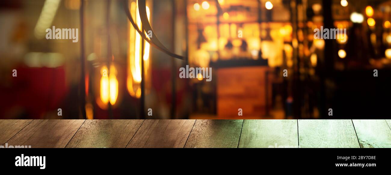 top of wood table with blur bar or pub with dark night party orange light city interior banner background Stock Photo