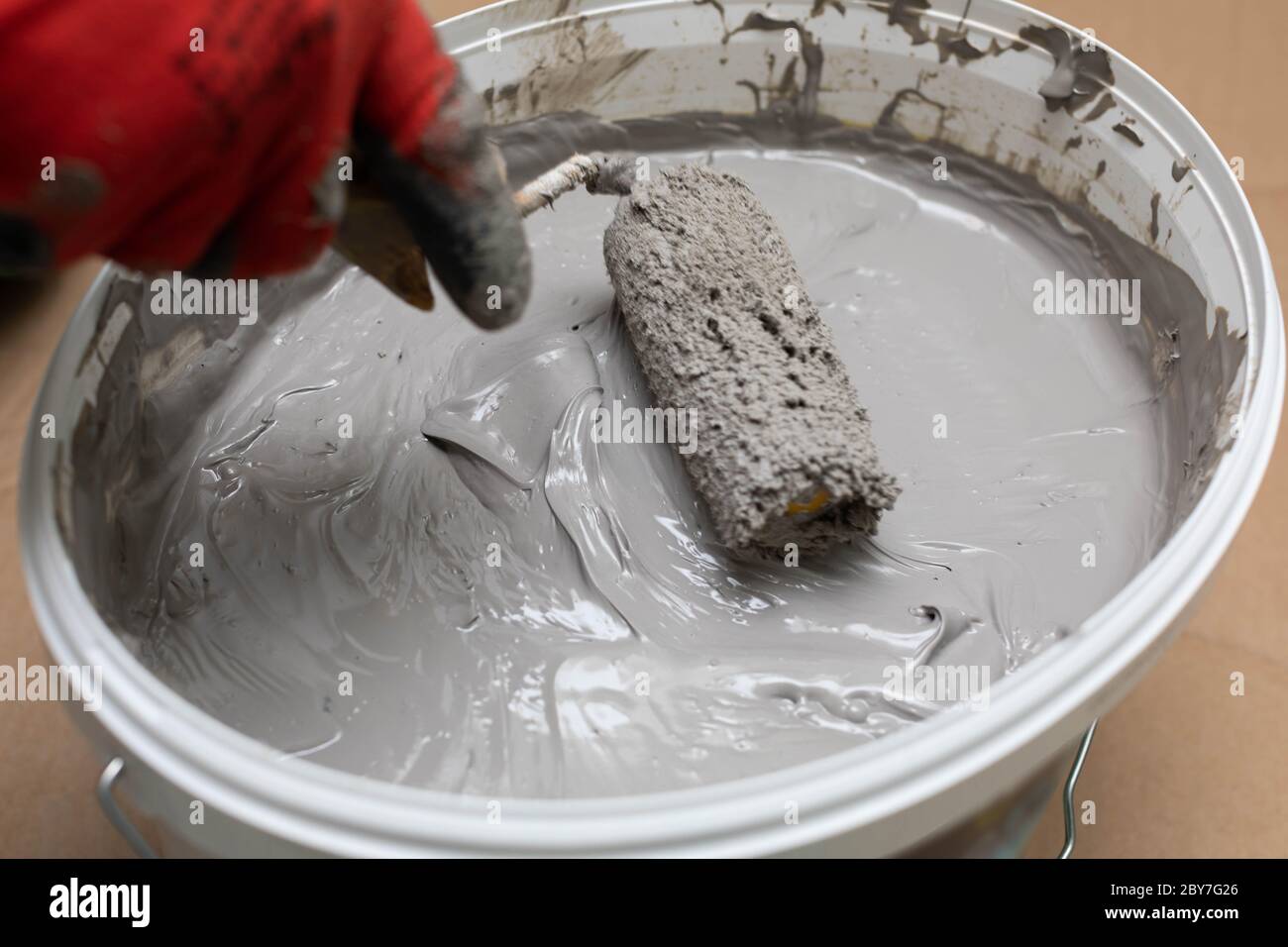 A professional construction worker soaks a paint roller in a bucket