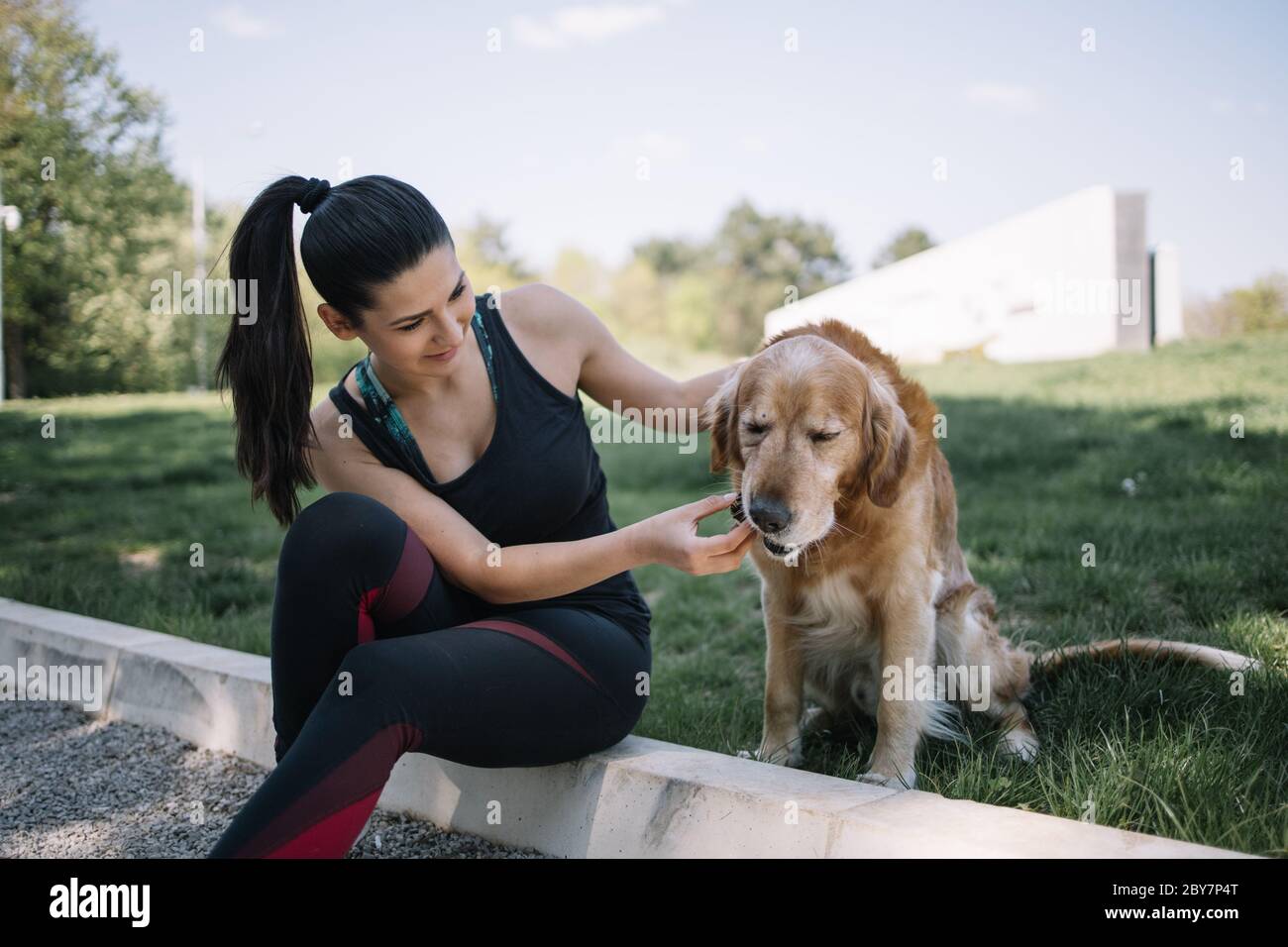 Brunette girl in sportswear sitting on ground with dog Stock Photo