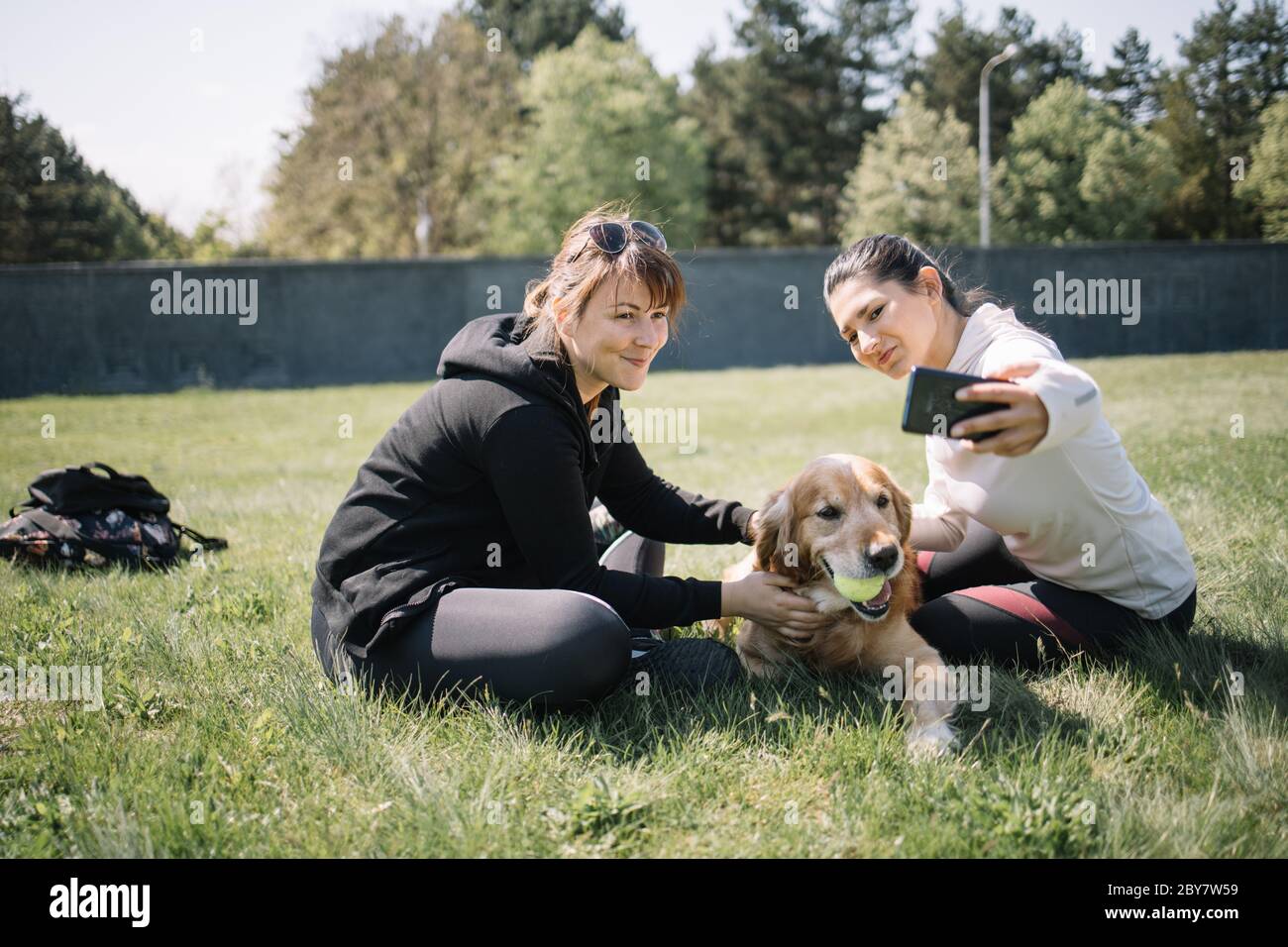 Smiling women sitting in park with dog and taking selfie Stock Photo ...