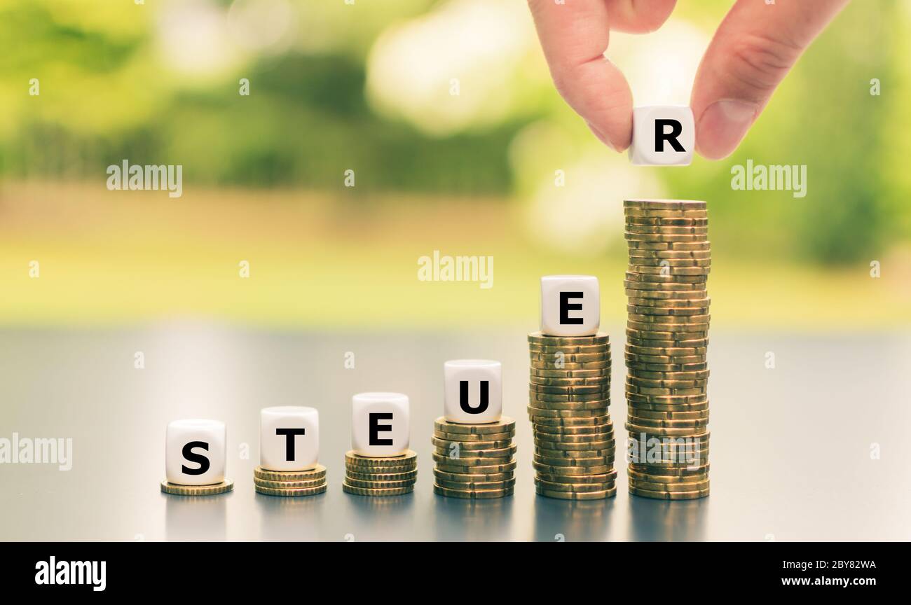 Dice form the German word "Steuer" ("tax") on increasing high stacks of coins. Stock Photo