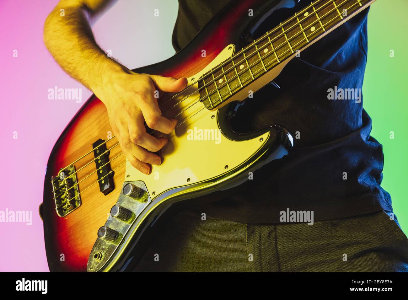 Close up musician hands playing bass guitar on gradient studio
