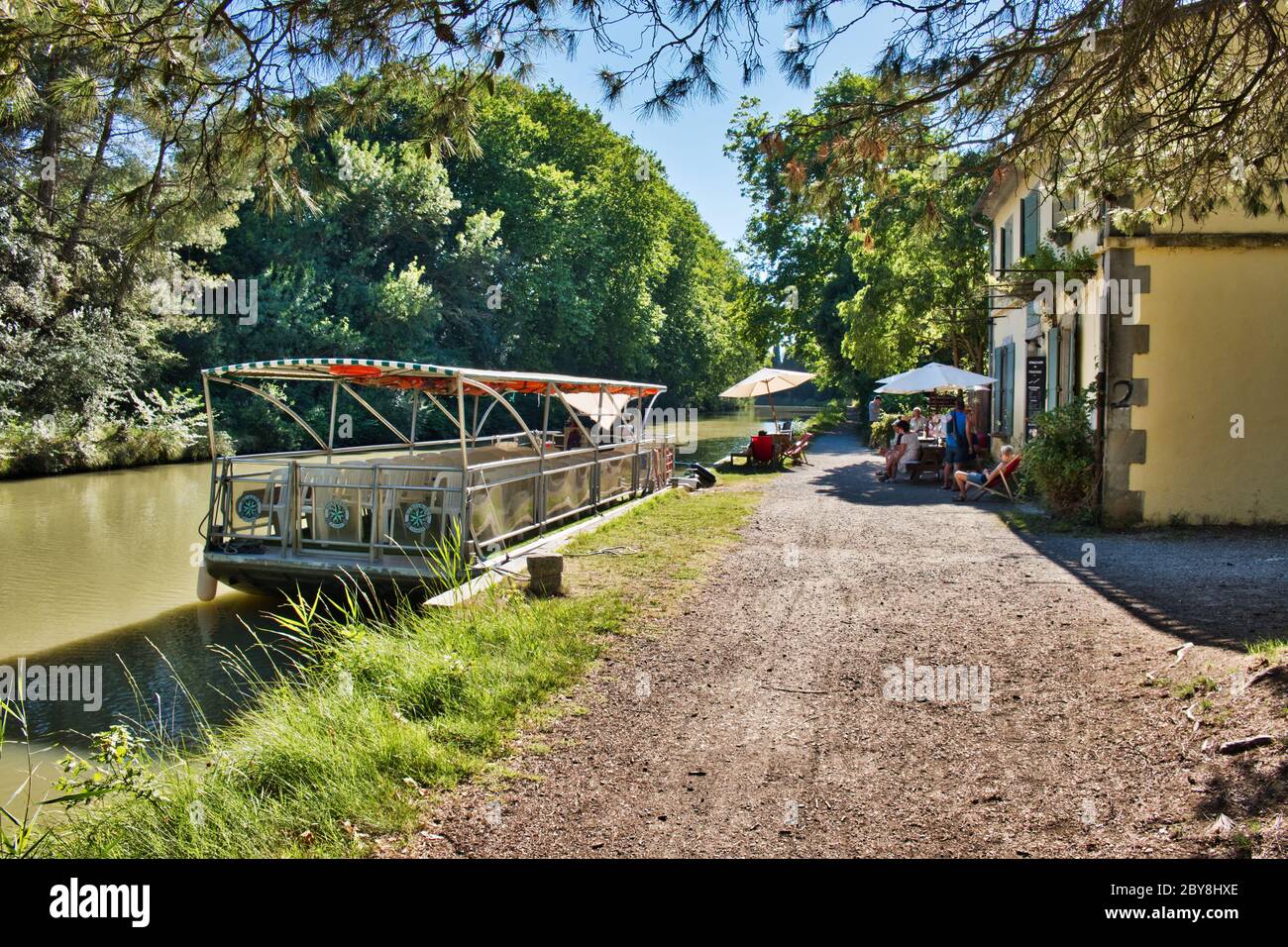 Carcassonne Aude France 07/11/19 Canal du Midi tow path and lock keepers cottage. Canal tour boat moored beside a cafe. Hoiday makers enjoying a cool Stock Photo