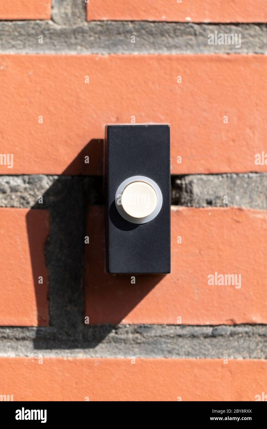 A close up straight portrait of a black and white old plastic doorbell on a red brick wall. The device is ready to be used for someone to announce tha Stock Photo