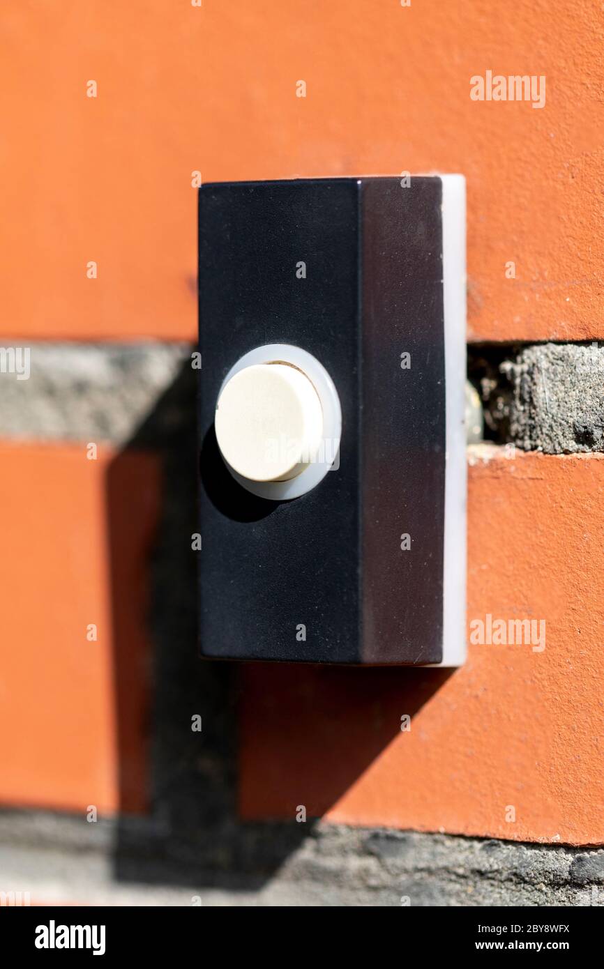 A close up portrait of an old electric doorbell on a red brick wall. The device is black with a white button to ring the bell. Stock Photo