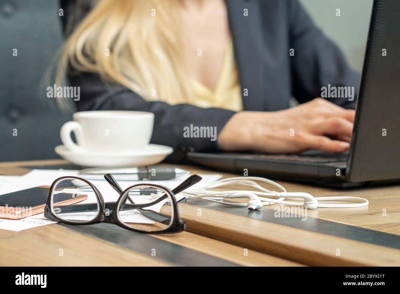 Eyeglass with coffee on office table on female business worker background. Stock Photo