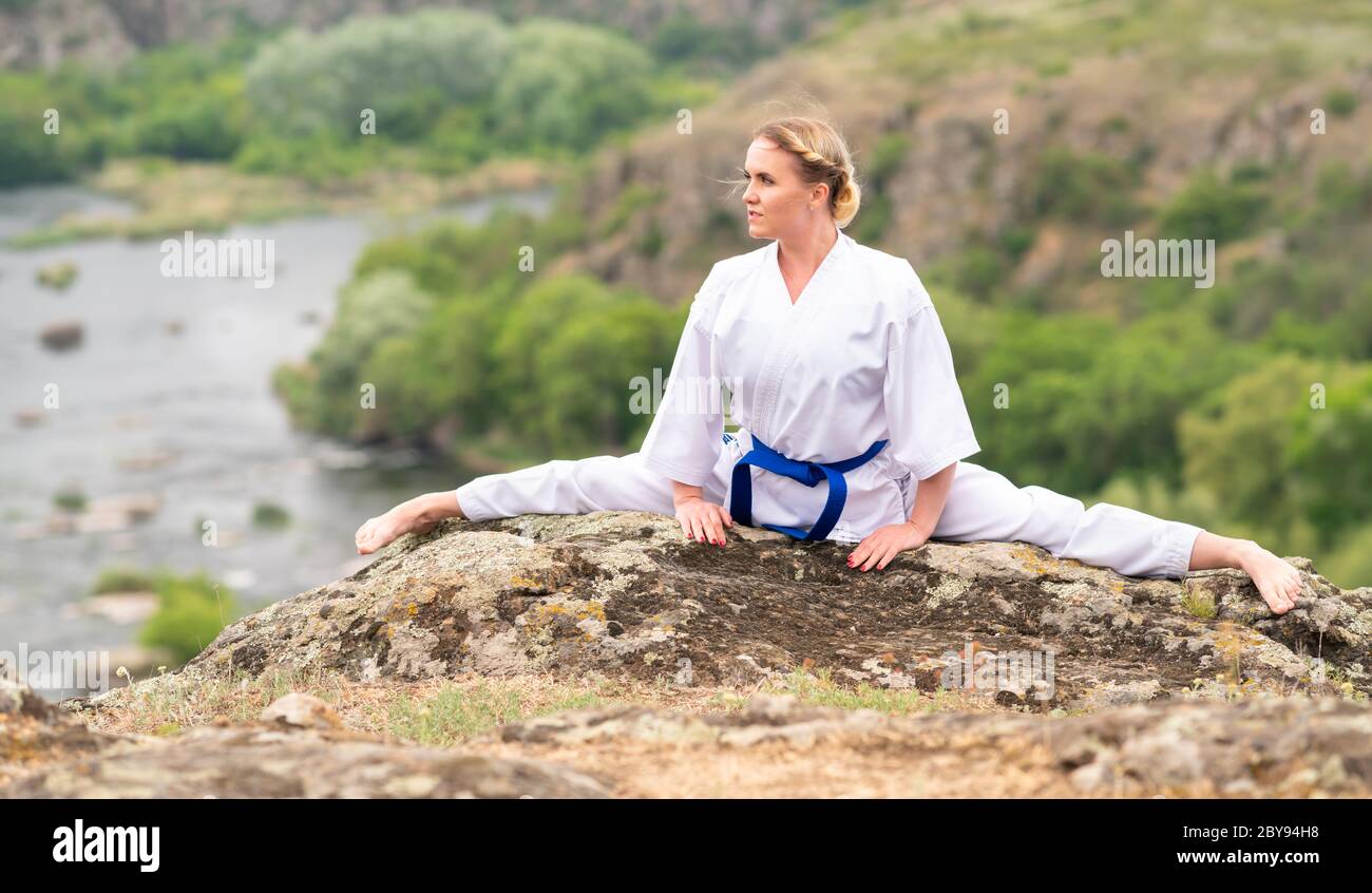 Supple athletic young woman doing the splits across a rock outdoors in a rural landscape with river below Stock Photo