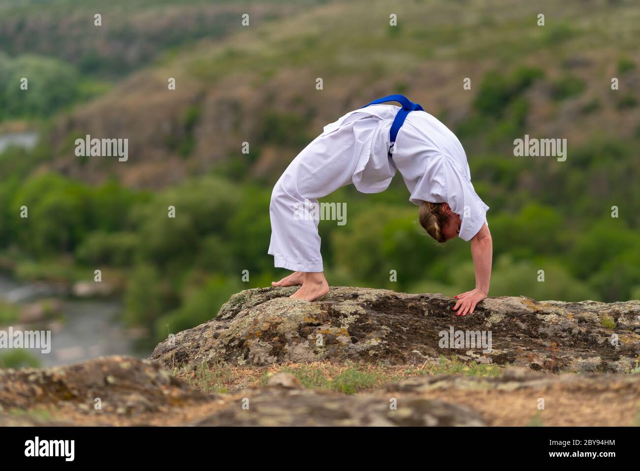 Supple fit woman doing a backward stretch outdoors to increase flexibility and mobility on a rock overlooking a valley below Stock Photo