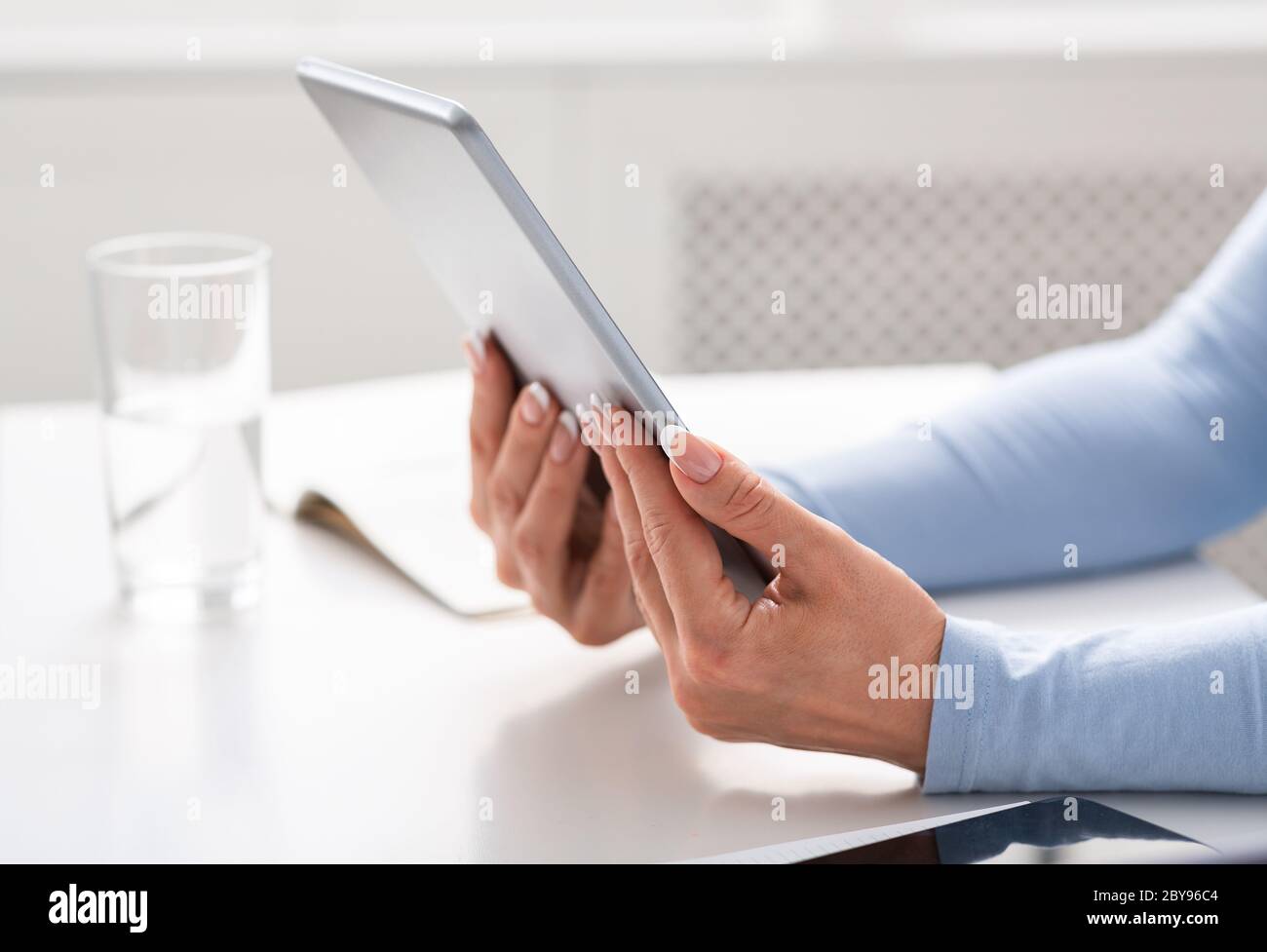 Online conference. Middle aged women hands holds tablet on white table Stock Photo