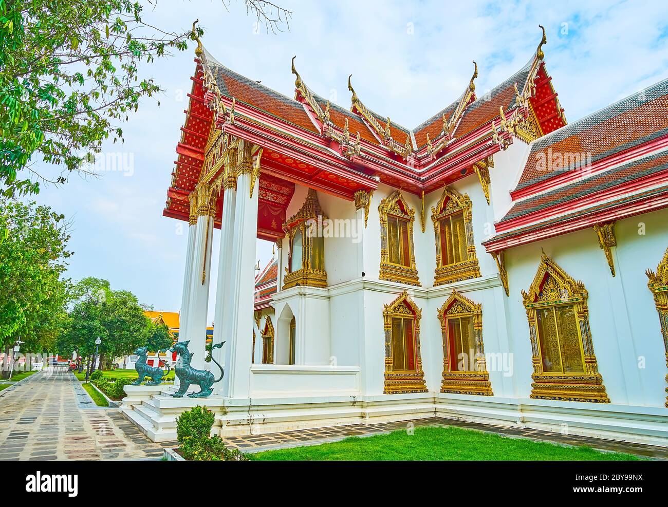 The porch of Phra Vihara Somdej pavilion is decorated with bronze singha lions, slender columns, gilt relief patterns and complex gable roof, Wat Benc Stock Photo