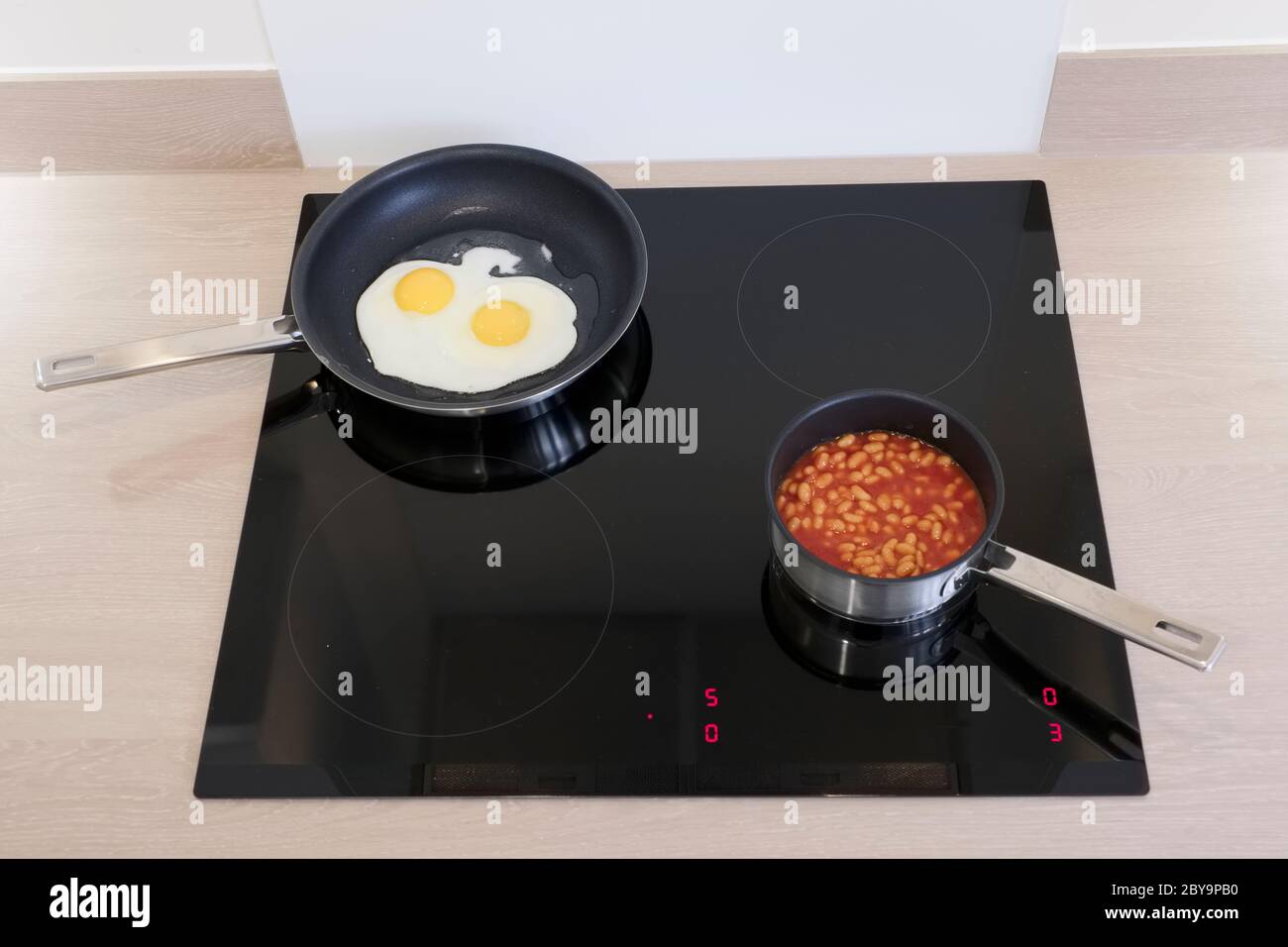 Fried eggs and baked beans cooking induction hob Stock Photo Alamy