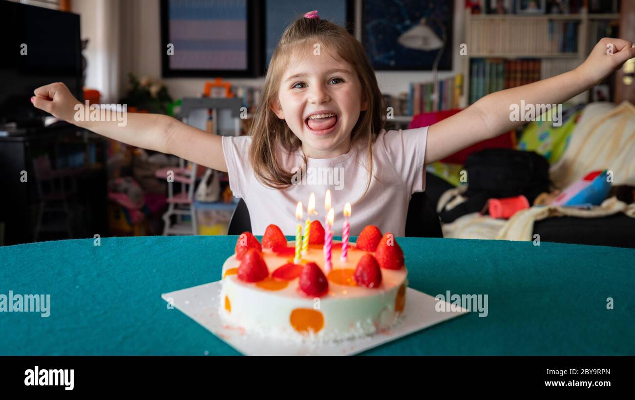 Happy exuberant little girl celebrating her birthday with a fruity strawberry cake and five candles cheering as she laughs at the camera Stock Photo