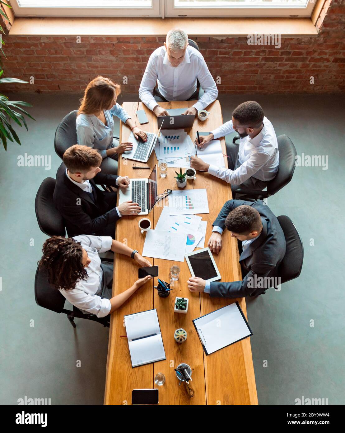 Business Colleagues Working Using Gadgets Sitting In Modern Office, Above-View Stock Photo