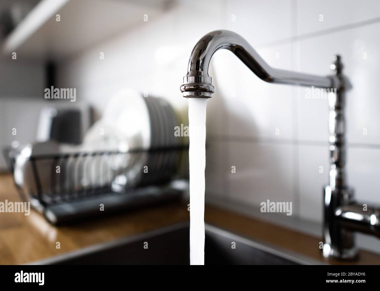 Water flowing out of a kitchen stainless steel tap into the sink. Wasting water by leaving a chrome faucet tap running. Overusing household water Stock Photo