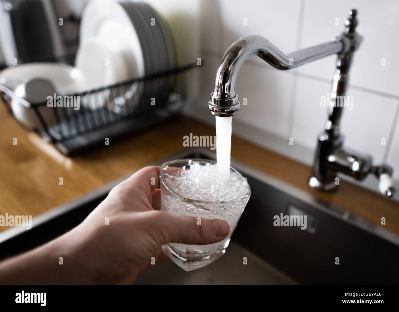 male's hand pouring water into the glass from chrome faucet to drink