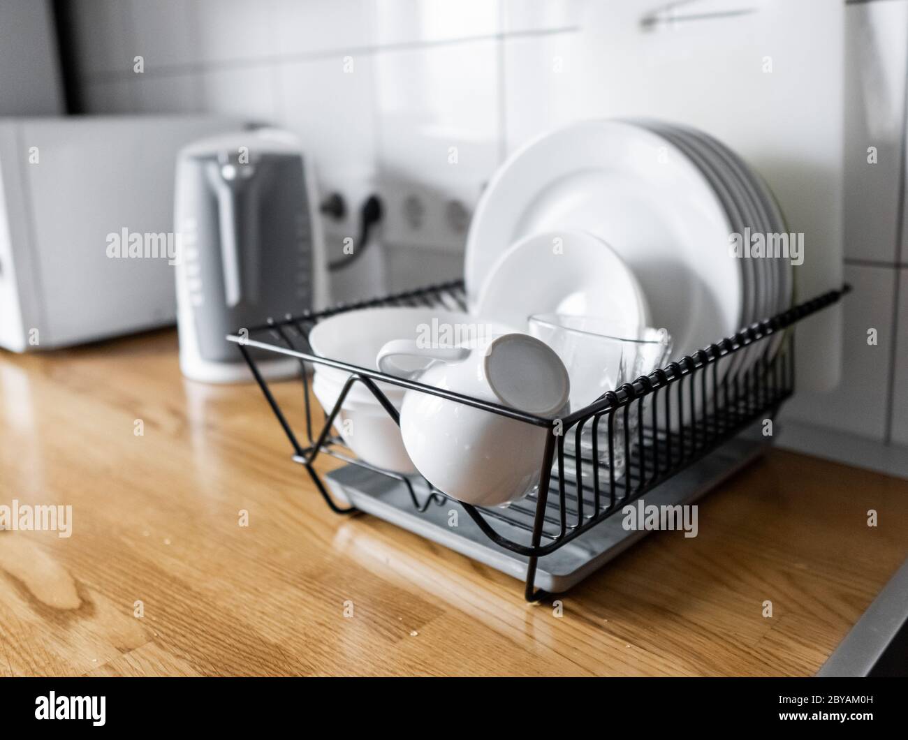 Dish rack holds many dishes and cups against wooden countertop, white