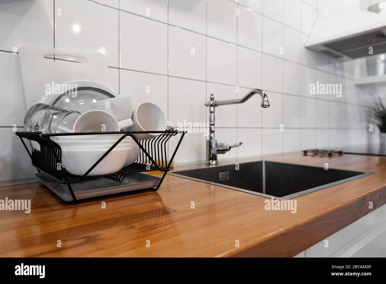 https://c8.alamy.com/comp/2BYAM0P/dish-rack-holds-many-dishes-and-cups-against-wooden-countertop-white-wall-tiles-sink-and-faucet-budget-and-lightweight-antimicrobial-dish-drainer-2BYAM0P.jpg