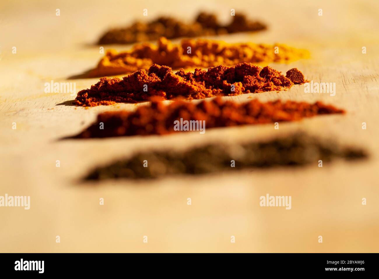 SPICE RACK: An arrangement of mini spoons with colorful herbal spices with a garlic clove rest on a wooden cutting board as ingredients for a recipe. Stock Photo
