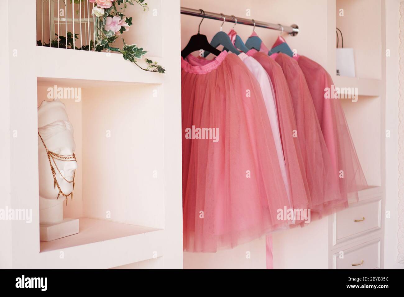 Dressing closet with pink clothes is arranged on hangers. The wardrobe is full of pink skirts, accessories on the shelves. Stock Photo