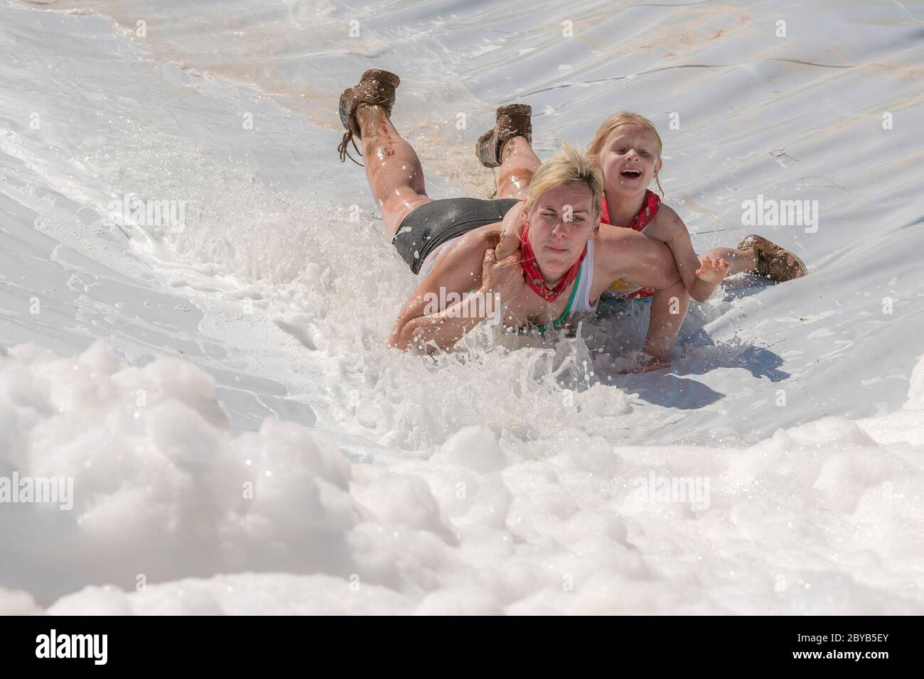 Poley Mountain, New Brunswick, Canada - June 10, 2017: Participating in the annual fundraiser 'Mud Run For Heart'. A woman and child slide down a foam Stock Photo