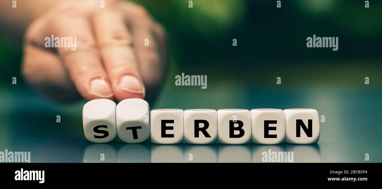 Hand turns dice and changes the German word 'sterben' ('die') to 'erben' ('inherit'). Stock Photo