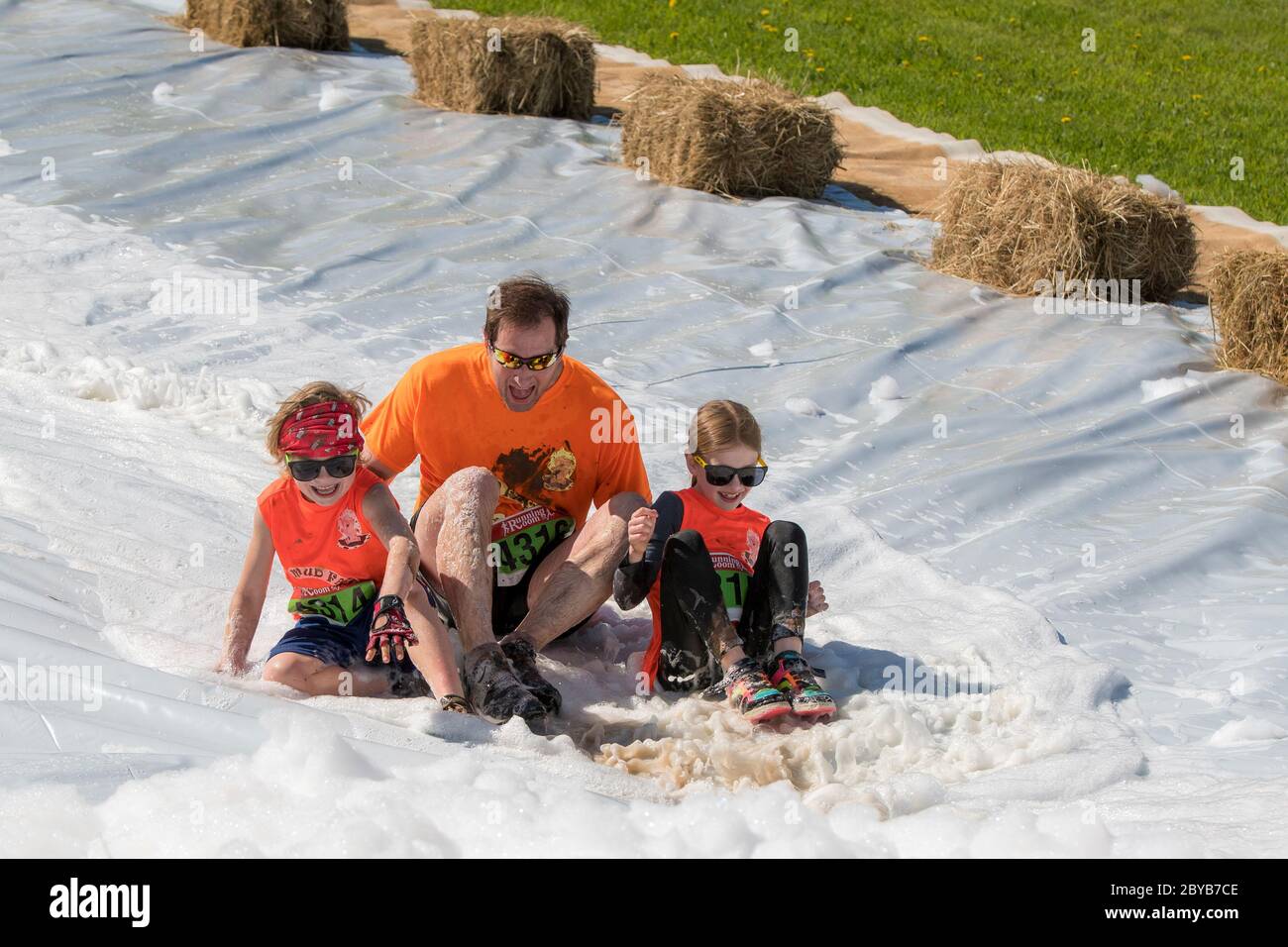 Poley Mountain, New Brunswick, Canada - June 10, 2017: Participating in the annual fundraiser 'Mud Run For Heart'. A man and two children slide down a Stock Photo