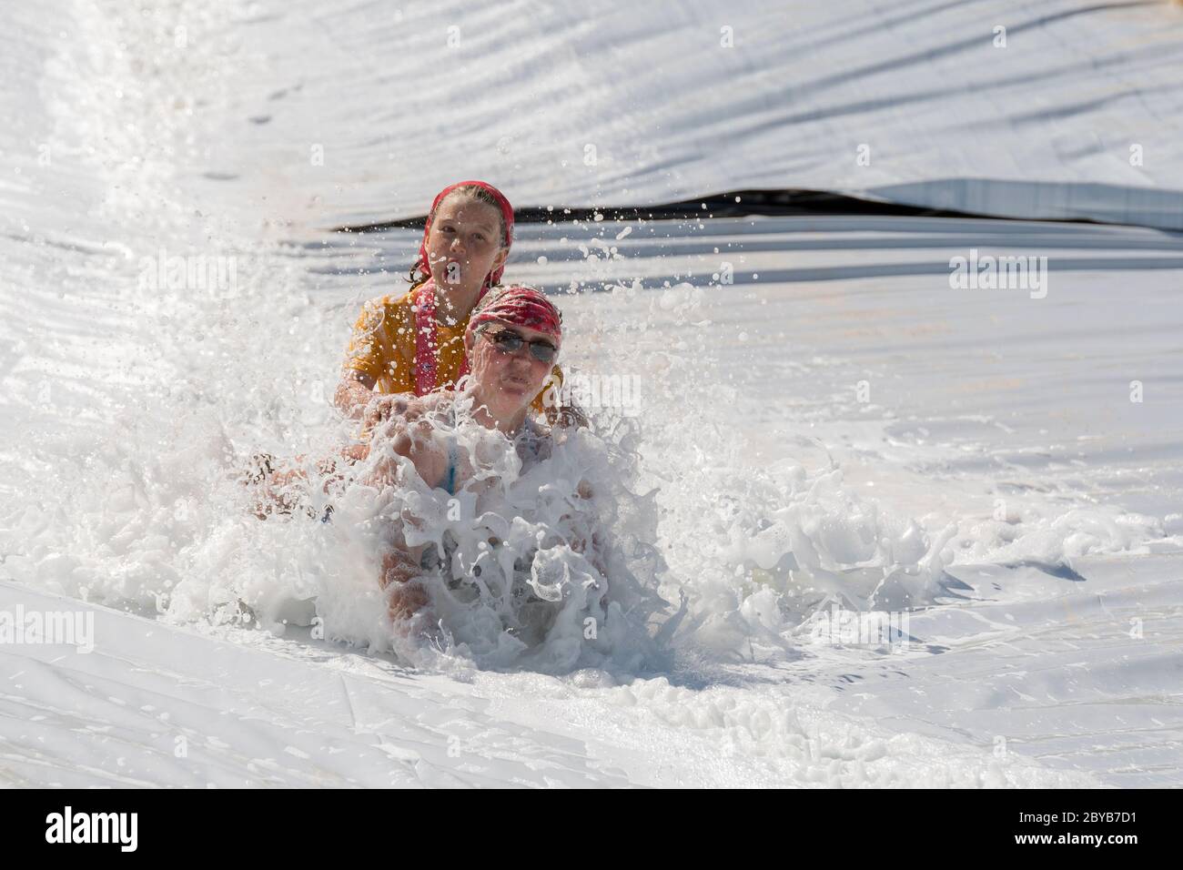 Poley Mountain, New Brunswick, Canada - June 10, 2017: Participating in the annual fundraiser 'Mud Run For Heart'. A woman and child slide down a foam Stock Photo