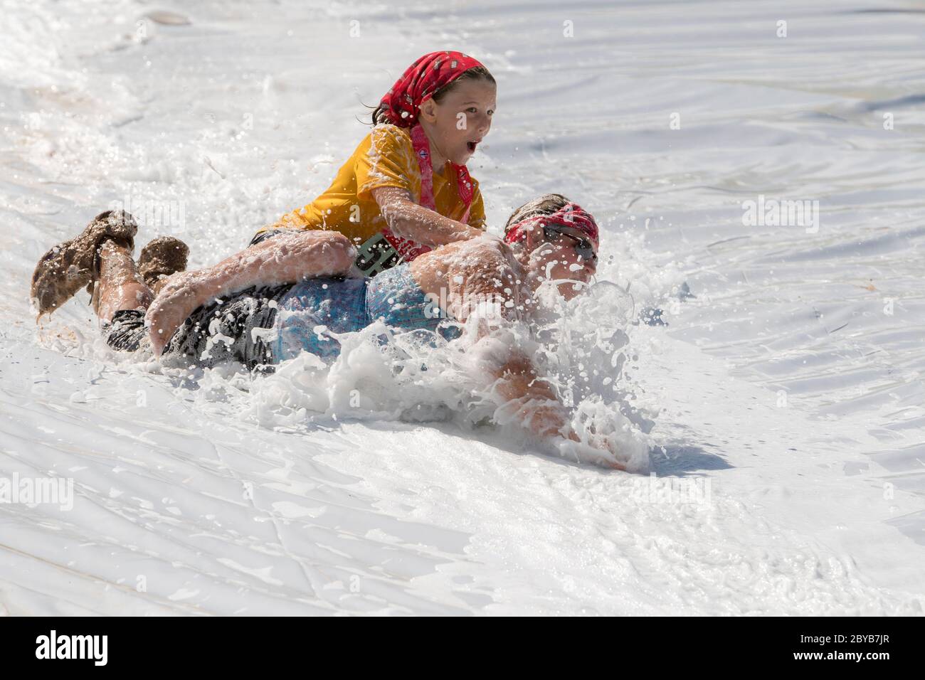 Poley Mountain, New Brunswick, Canada - June 10, 2017: Participating in the annual fundraiser 'Mud Run For Heart'. A woman and child slide down a foam Stock Photo