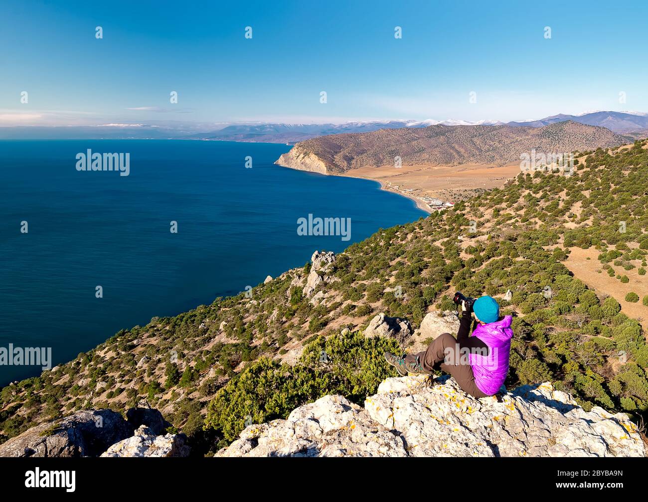 Young woman photographer taking photo of Black Sea on mountain peak in New World, Crimea Stock Photo