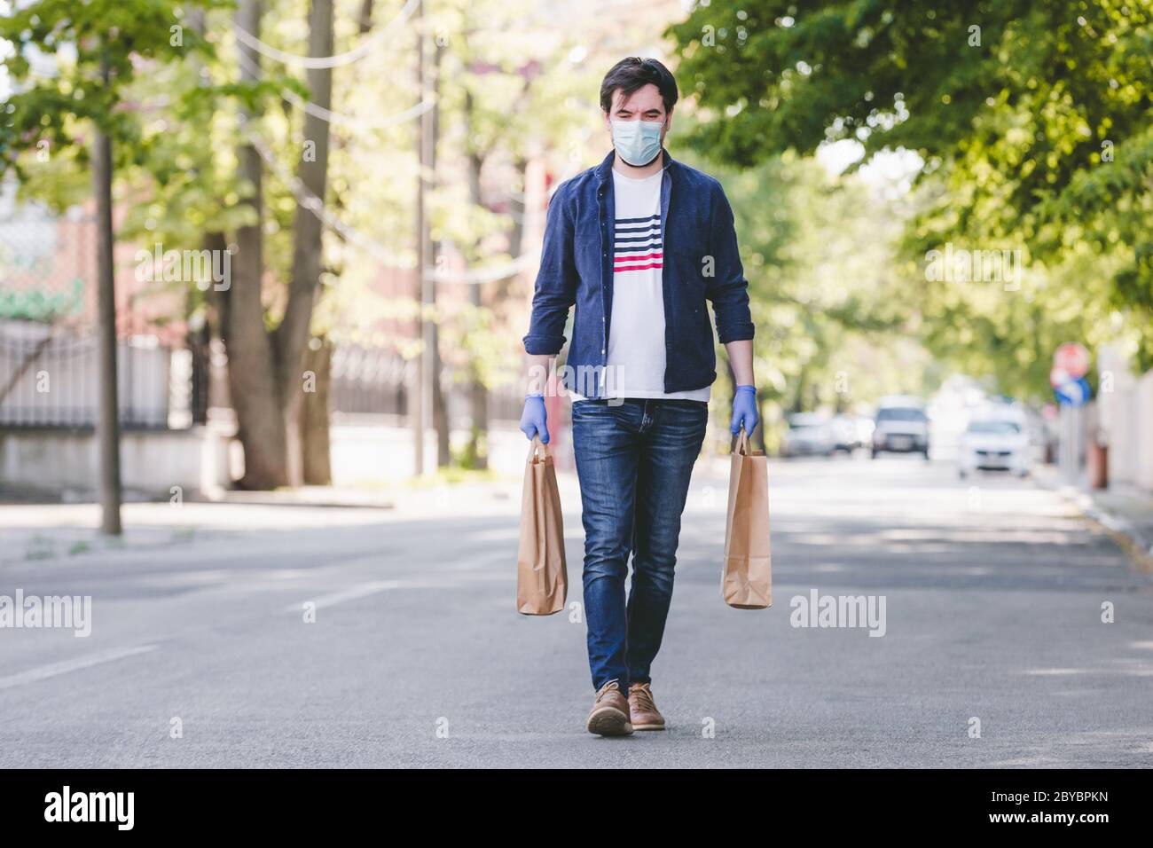 Courier in protective mask and medical gloves delivers takeaway food.        Delivery service under quarantine, disease outbreak, coronavirus covid-19 Stock Photo