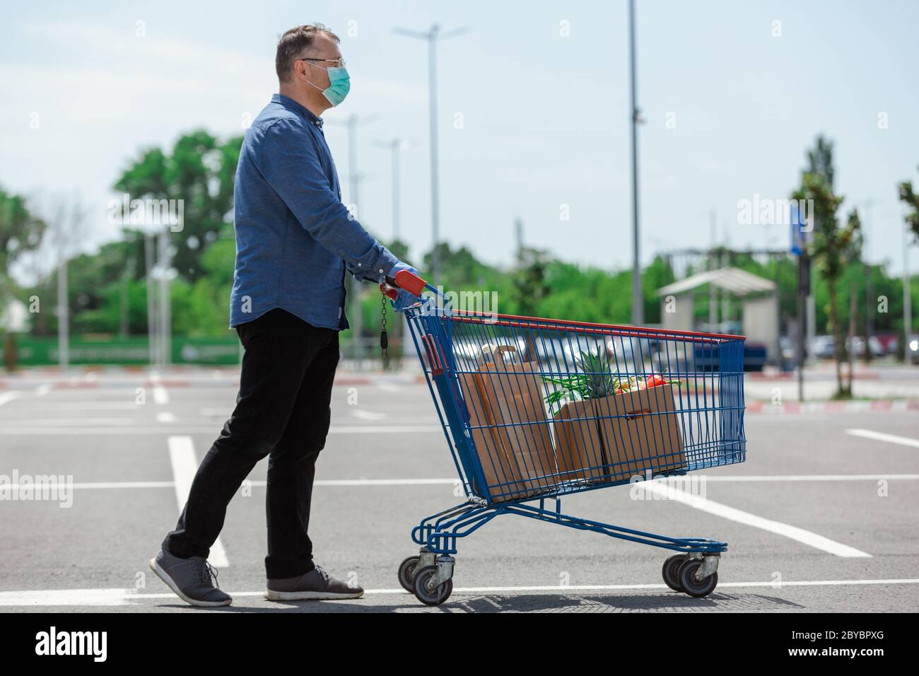 Senior man pushing a shopping cart full of bags and food box, man delivering food with protective mask and gloves Stock Photo