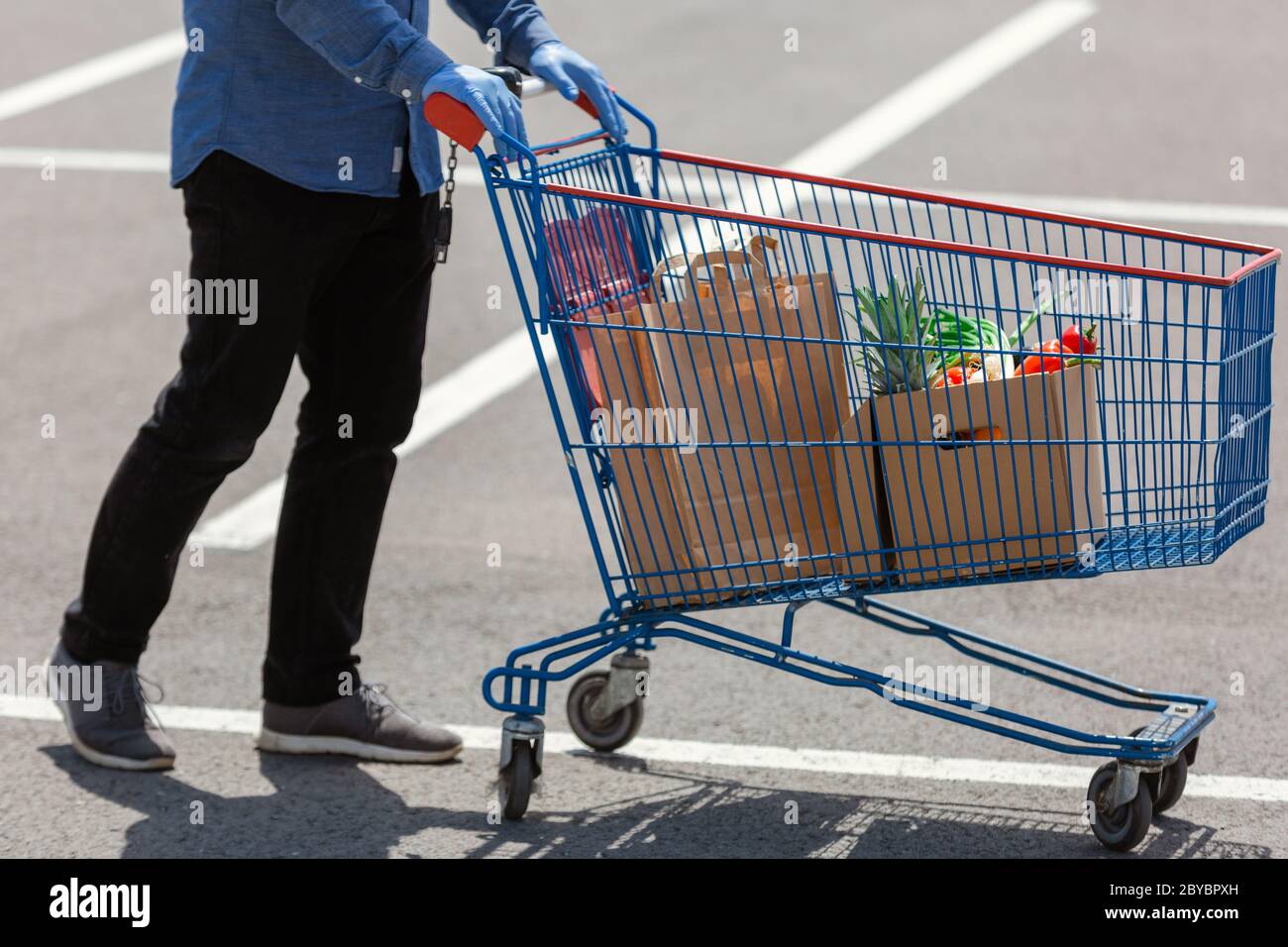 Senior man pushing a shopping cart full of bags and food box, man delivering food with protective  gloves Stock Photo