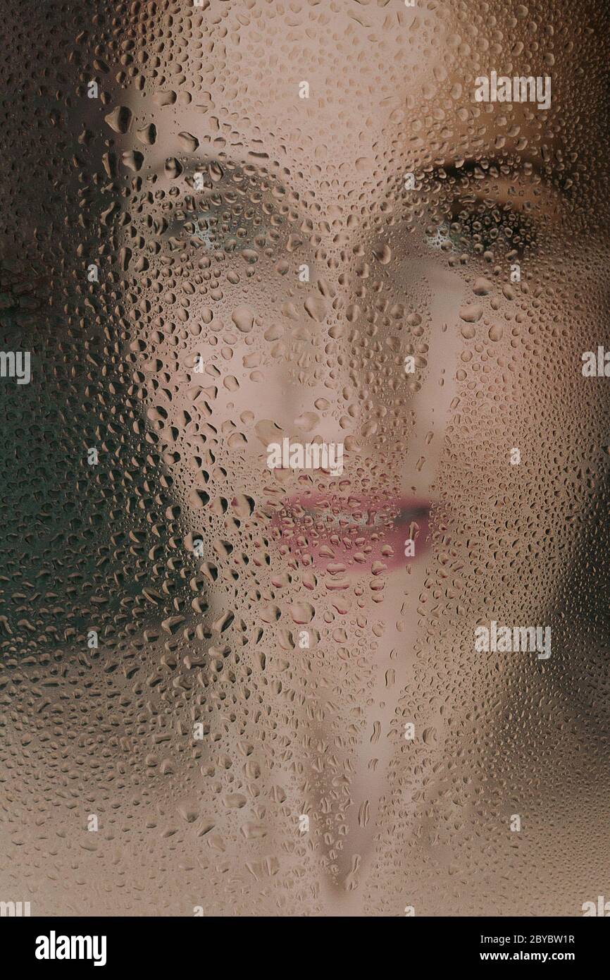 Portrait of a girl through wet glass with drops of water Stock Photo