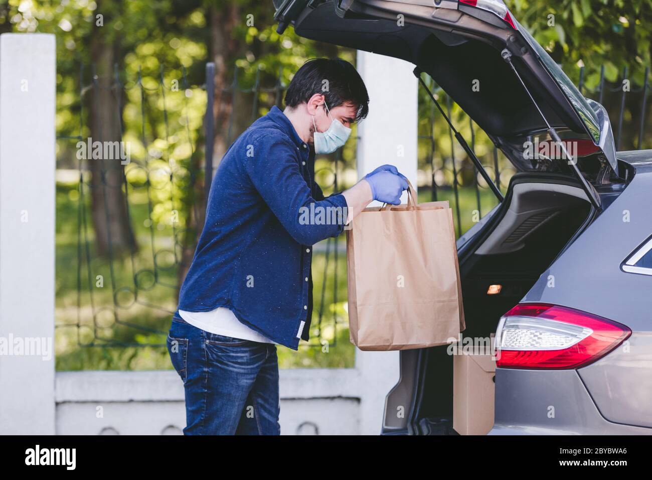 Delivery man putting paper bag with food in the car, food delivery man with protective mask and gloves Stock Photo