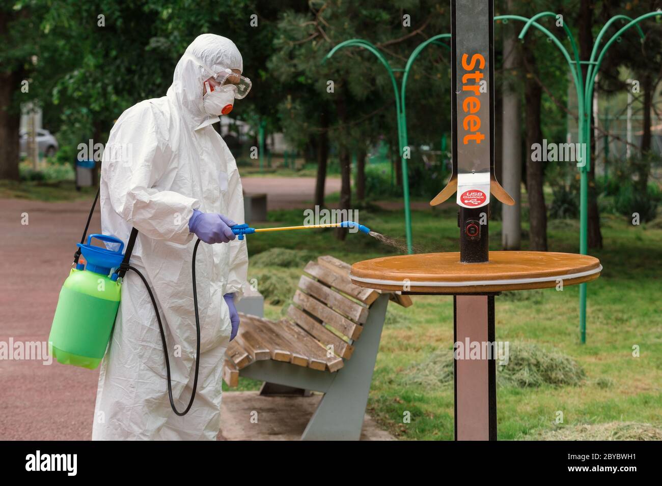 Man wearing protective suit disinfecting the solar charger with spray chemicals to preventing the spread of coronavirus, pandemic in quarantine city. Stock Photo