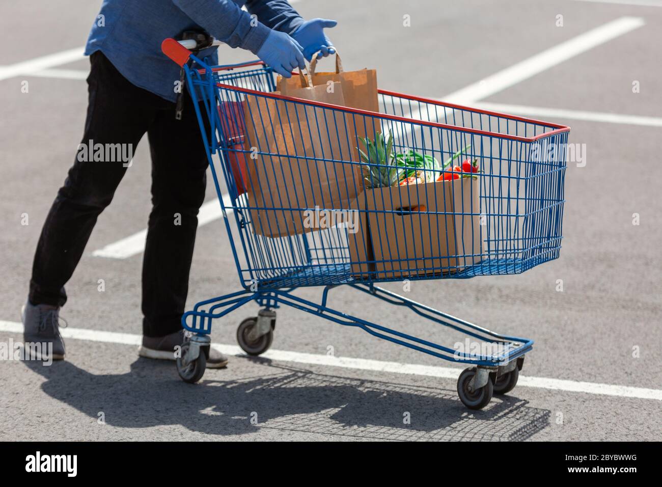 Senior man putting paper bag and box  with food in shopping cart, food delivery man with protective  gloves Stock Photo