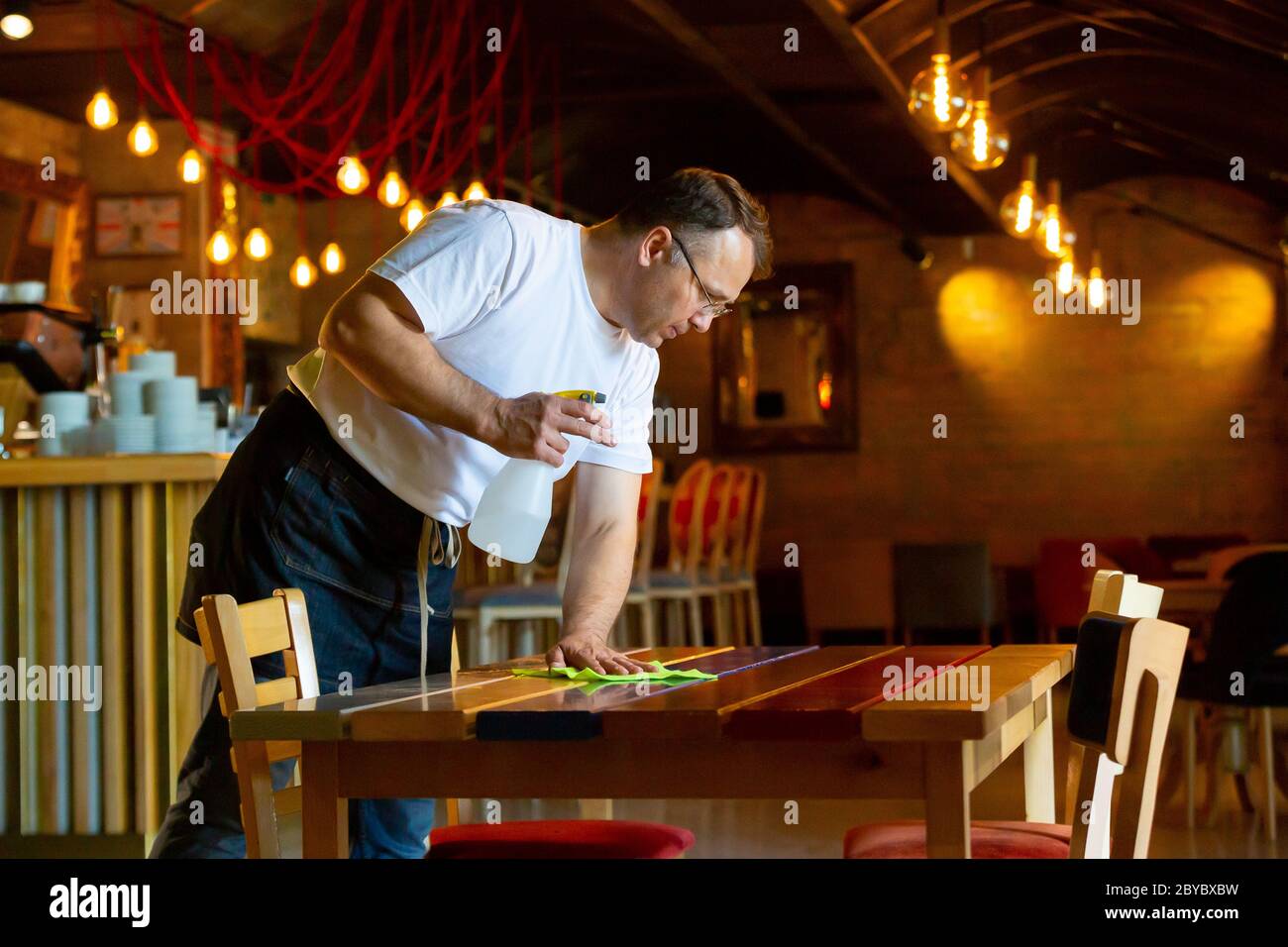 Waiter Cleaning the Table with Disinfectant Spray in a Restaurant Stock Photo