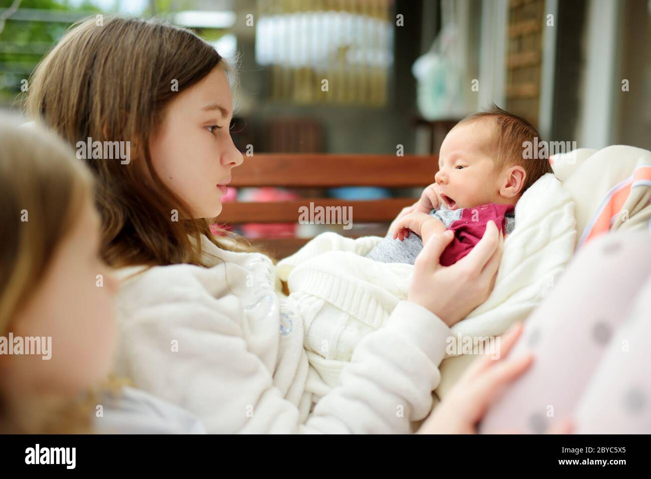 Two big sisters admiring their newborn brother. Two young girls holding