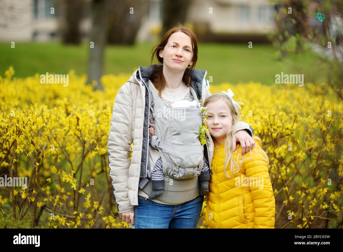 Young mother with a newborn in a baby carrier hugging her older