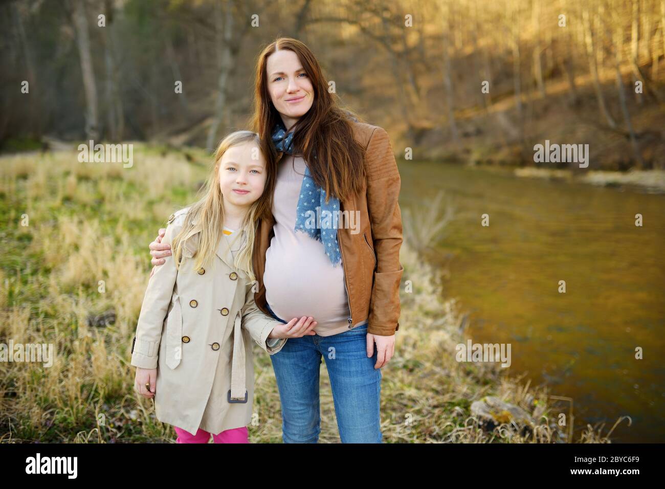Young pregnant woman hugging her older daughter. Cute young child having fun with her pregnant mom outdoors. Mother and her kid spending quality time Stock Photo